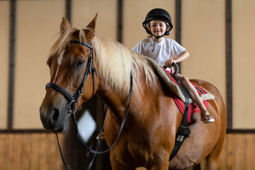 Smiling little girl in helmet learning horseback riding. .Happy child teaching equestrian on horse