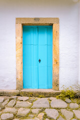 Blue door, stone door frame and stone floor. Colorful colonial-style houses in the Historic Center of Paraty; Portuguese base architecture: white walls with roofs and colorful windows and doors.