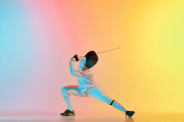 Fototapeta na wymiar Young man, male fencer with sword practicing in fencing over gradient pink-yellow background in neon light. Sportsman shows fencing technique