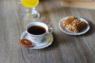 Cup of tea, plates with cookies, glass of orange juice, books, reading glasses, bowl of fruit and candles on the table. Selective focus.
