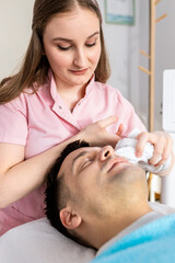 Obraz na płótnie Canvas Beautician doing face treatment in beauty salon to a man.