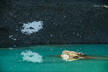 Beautiful scenic landscape with mossy rock in turquoise mountain lake. Azure glacial lake in sunlight. Colorful scenery with mossy stone above clear water surface. Sunny lake and stony mountain.