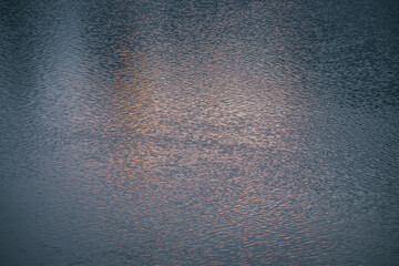 Texture of magenta calm water of lake in sunrise. Meditative ripples on water surface. Nature minimal background of pink lake in sunset. Natural backdrop of clear water. Full frame of lake fragment.
