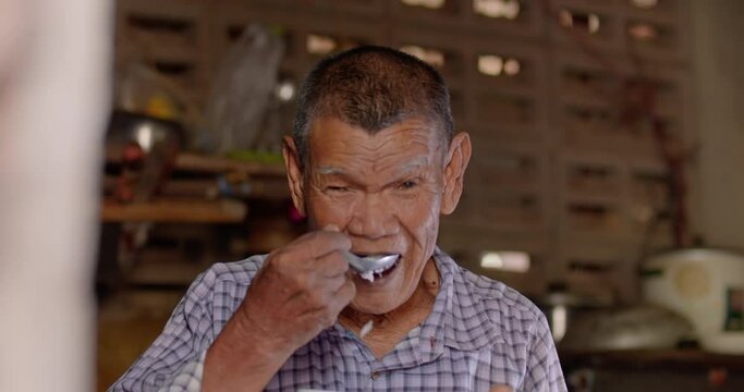 Slow motion of an Asian man who is  a poor elderly native and works as a wage earner in a farm, live in a poor house, eating rice. Use in documentary concept.