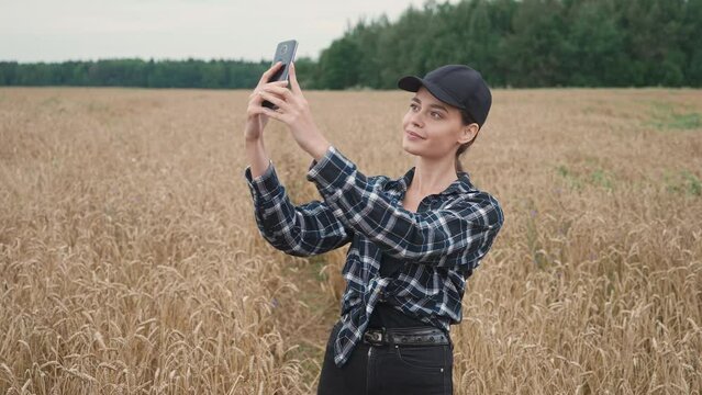 Countryside, woman farmer standing in a field of rye and takes selfie pictures on a smartphone, investigating plants.