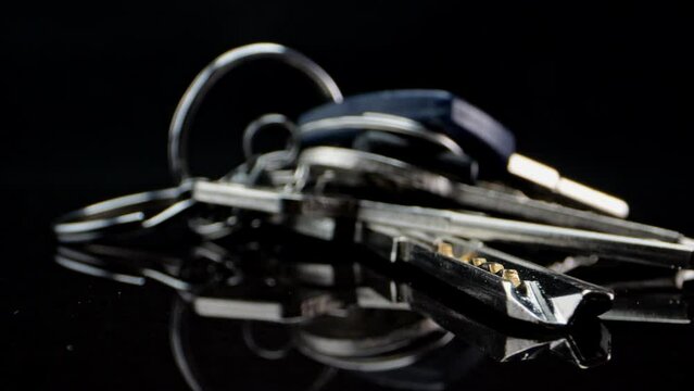 A bunch of keys lies on a black mirror surface and spins slowly. Macro shot