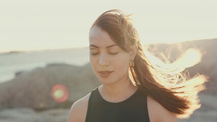 Meditation, peace and yoga with woman at beach for spiritual, mindfulness and fitness. Wellness, freedom and windy with girl breathing on rocks in nature for faith, summer break and calm mindset