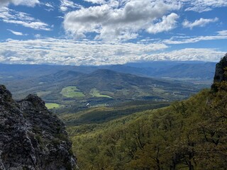 Naklejka premium Landscape of a mountainous area with green slopes, trees, spring flowers and a blue sky with white clouds.