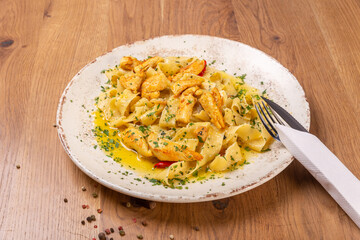 Pappardelle pasta with chicken fillet, garlic and chili sprinkled with parmesan cheese and chopped parsley, close up. The dish is served with cutlery on a wooden table.
