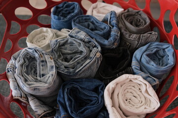 Different colors of rolled denim jeans are in a red laundry basket.