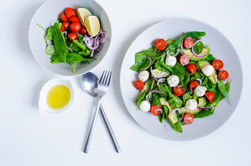 top view of delicious diet salad  with cherry tomatoes, avocado, spinach leaves, Mozzarella and red onion with olive oil dressing served on plate