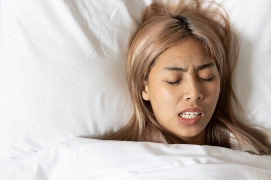Tired and stressed Asian woman with colored hair sleeping, having bad dream, nightmare with bruxism or grinding teeth
