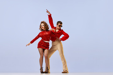 Young beautiful couple of dancers in bright retro fashion clothes, stage costumes dancing over lilac color background. Concept of music, art, dance, retro