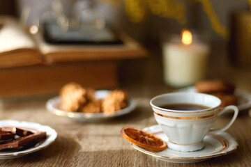 Scented candles, chocolate, cookies, cup of tea, books, e-reader, glasses and flowers on the table. Hygge at home. Selective focus.