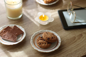 Scented candles, chocolate, cookies, cup of tea, books, e-reader, glasses and flowers on the table. Hygge at home. Selective focus.