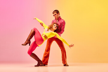 Young stylish emotional man and woman, professional dancers in retro style clothes dancing disco dance over pink-yellow background. 1970s, 1980s fashion, music concept