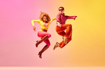 Fototapeta na wymiar Stylish expressive excited couple of professional dancers in retro style clothes dancing disco dance over pink-yellow background. Concept of 70s, 80s fashion style, music and emotions
