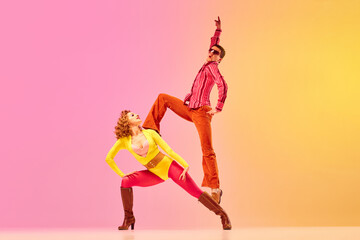 Young stylish emotional man and woman, professional dancers in retro style clothes dancing disco dance over pink-yellow background. 1970s, 1980s fashion, music concept