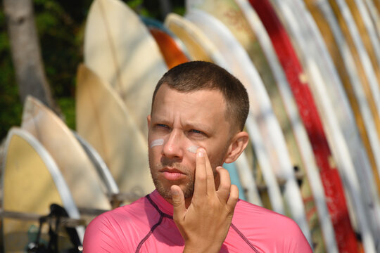 Man surfer applies protective zinc on his face. Preparing to surf. Best protection from active sun and UV while surfing. Eco-friendly product that is safe for corals in ocean.