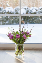 Purple bouquet of tulips near a large window overlooking the winter garden.