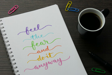 FEEL THE FEAR AND DO IT ANYWAY colorful lettering in notebook with cup of espresso and pen on black wooden desk