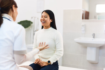 A healthy Asian female patient laughing with a female doctor at the clinic.