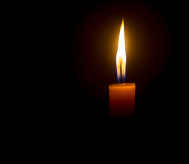 A single burning candle flame or light glowing on an orange candle on black or dark background on table in church for Christmas, funeral or memorial service with copy space