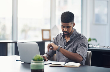 Good time management allows you to accomplish more. Shot of a young businessman checking the time while working on a laptop in an office.