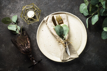 Table setting with white craft plate, cutlery and decorations at black stone table. Top view image.