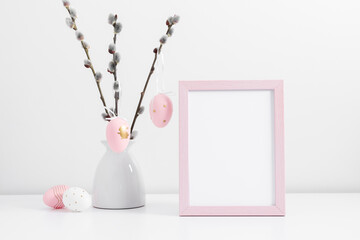 Easter holiday composition. Empty pink photo frame mockup, vase with willow branches, easter eggs,...