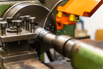 A close up of a lathe machine with an orange safety guard, machine is cutting a piece of metal.