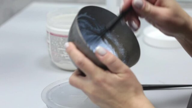 Hand mixing hair dye in a plastic bowl in a beauty salon. The hairdresser is preparing a dye for dyeing hair with pigment in a bowl. Color your hair at the barbershop