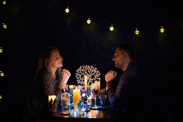 A romantic couple sharing a candlelit dinner. The dimly lit room creates an intimate atmosphere while the candles on the table add a touch of elegance to the setting.