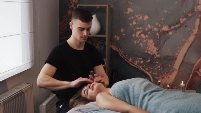 portrait of male massage therapist's hands giving gentle facial massage to young woman in a massage room with soft lighting