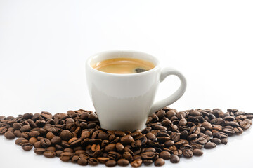 A cup of espresso in a pile of roasted coffee beans on a white background.
