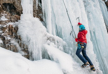 Ice climber dressed in warm winter climbing clothes, safety harness and helmet climbing frozen...