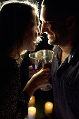 A romantic close-up of an elegant couple holding wine glasses, illuminated with moody backlight and smoke, with candles on the table creating an intimate atmosphere.
