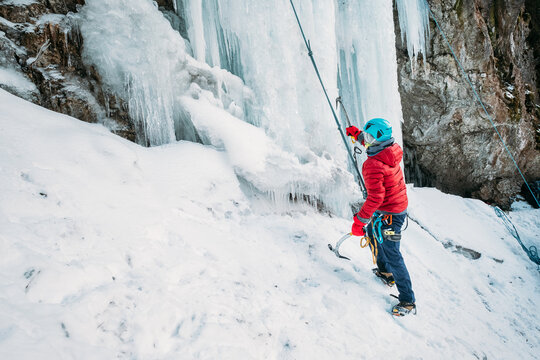 Ice climber dressed warm winter climbing clothes, safety harness and helmet under the frozen waterfall. Active people and sporty activities concept image.