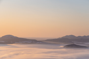 Fototapeta na wymiar 霞んだ夜明けの山々のシルエットと靄に覆われた湖。