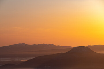 Fototapeta na wymiar オレンジ色の夜明けの空と遠くの山々のシルエット。