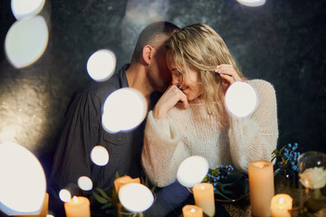 A romantic couple in a dimly lit restaurant with flickering candles, the man whispering sweet...
