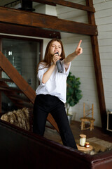 A happy woman sings into a microphone and imagines that she is on stage in a home interior.