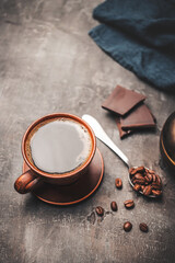 Black coffee drink in a clay cup, chocolate pieces and coffee beans in a spoon on dark background