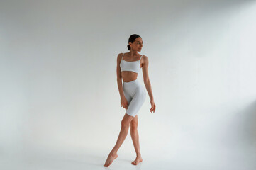 In white fitness clothes. Young caucasian woman with slim body shape is indoors in the studio