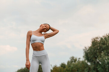 Warm up exercises. Young caucasian woman with slim body shape is in the fitness clothes outdoors