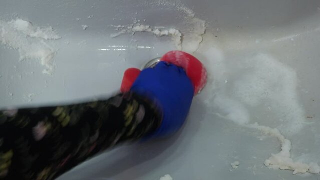 Female hand in a glove cleans the sink in the bathroom using baking soda and a sponge for washing