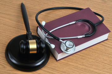 Concept d'erreur médicale avec un stéthoscope posé sur un livre et un marteau de juge sur un fond en bois - obrazy, fototapety, plakaty