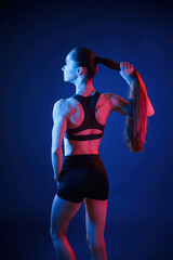Rear view. Beautiful muscular woman is indoors in the studio with neon lighting