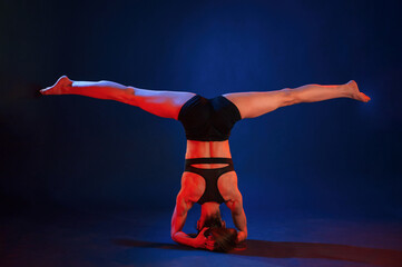 Doing head stand. Beautiful muscular woman is indoors in the studio with neon lighting