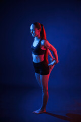 Fototapeta na wymiar Preparing for sportive exercises. Warm up exercises. Beautiful muscular woman is indoors in the studio with neon lighting